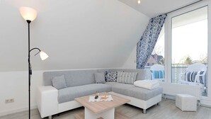 Una sala moderna con un sofá seccional, una mesa de centro, una lámpara de pie y un ventanal con vistas al exterior.