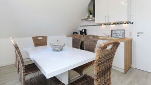 Una cocina moderna con armarios blancos, una encimera blanca y sillas de mimbre alrededor de una mesa rectangular.