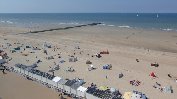 Une plage avec des tentes, des parasols et une longue jetée qui s’avance dans l’eau.