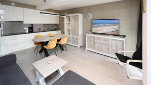 Un salon moderne avec un coin repas, un téléviseur fixé au mur et une vue sur la plage.