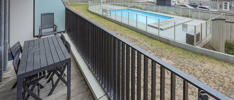 A balcony with a pool, wooden deck, and a view of surrounding buildings.