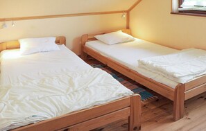 Dos camas individuales de madera con ropa de cama blanca en una habitación con techo inclinado y una ventana.