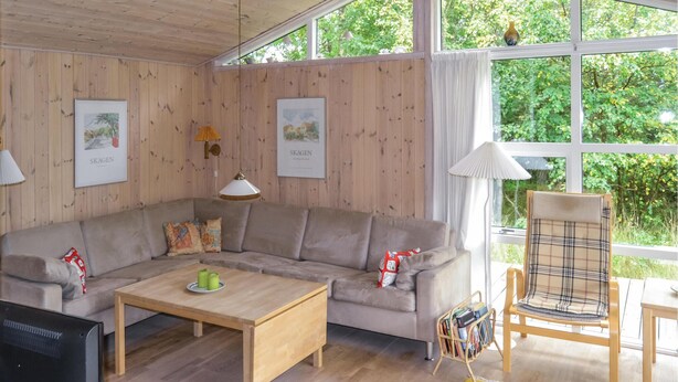 A cozy living room with a wooden panel wall, a grey sofa, a wooden coffee table, a TV, and a window with a view of greenery. - Gorgeous home in ålbæk with sauna (Ålbæk)