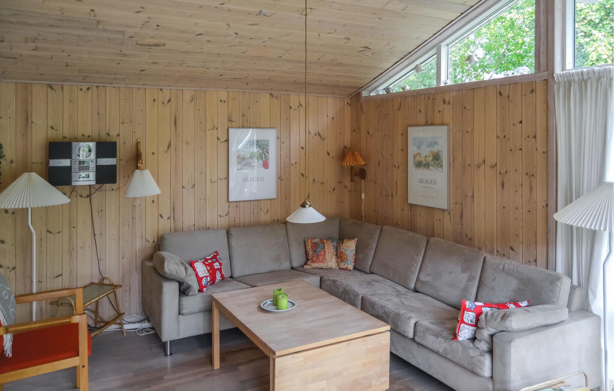 Un salon chaleureux avec un plafond en bois, un canapé gris, une table basse en bois et deux lampes fixées au mur.