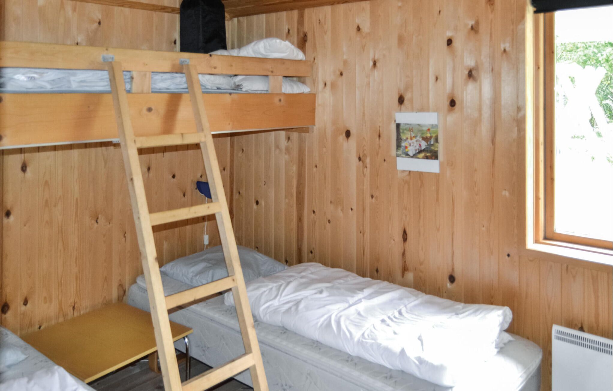A bunk bed room with a wooden ladder, a small table, and a window.