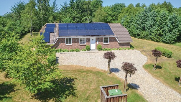 Une maison avec des panneaux solaires sur le toit, entourée d’une allée en gravier et d’arbres.