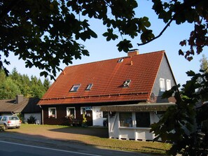 Un bâtiment à deux étages, doté d’un toit recouvert de tuiles rouges, d’un petit porche et d’une enseigne indiquant qu’il s’agit d’une maison d’hôtes.
