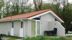Un edificio de un piso con techo inclinado, una puerta principal y un pequeño patio con mesa y sillas.