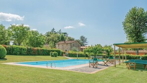 A swimming pool with a deck, surrounded by grass and trees, with a stone building in the background. - Beautiful home in Vicchio -FI- (Vicchio -FI-)