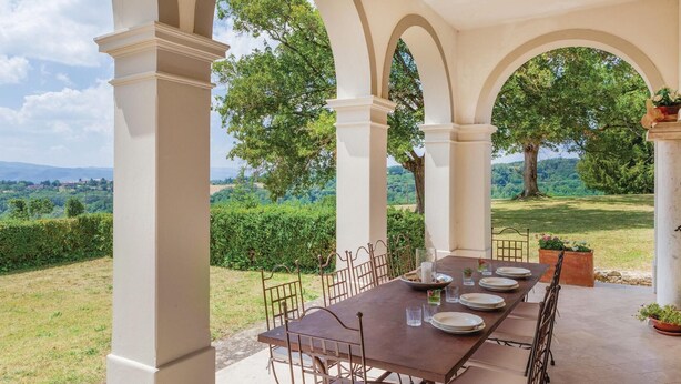 An outdoor dining area with a table set for four, surrounded by white columns, overlooking a lush landscape with trees and hills. - Beautiful home in Vicchio -FI- (Vicchio -FI-)