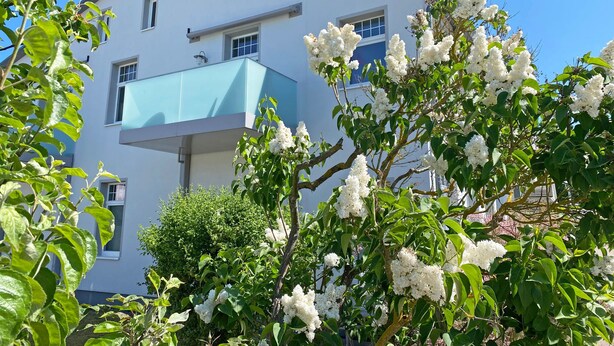 En moderne bygning med balkon og hvide blomster i forgrunden.