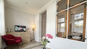 En moderne stue med en rød lænestol, et fjernsyn, en lampe og en vase med blomster.