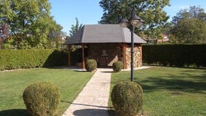 A stone gazebo with a tiled roof, surrounded by well-manicured hedges and a stone pathway leading to it. - Studio with internet, barbecue and pavilion (Gyenesdiás)