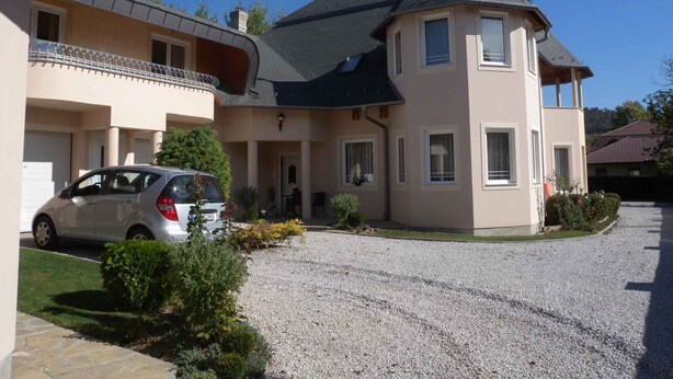 A two-story house with a gravel driveway and a parked car. - Studio with internet, barbecue and pavilion (Gyenesdiás)