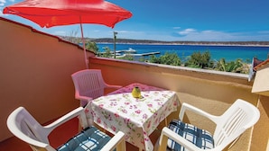 A balcony with a table and chairs, a red umbrella, and a view of the sea and boats.