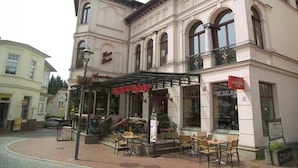 En bygning med en café i stueetagen, med udendørs siddepladser og en trappe op til øvre etage.