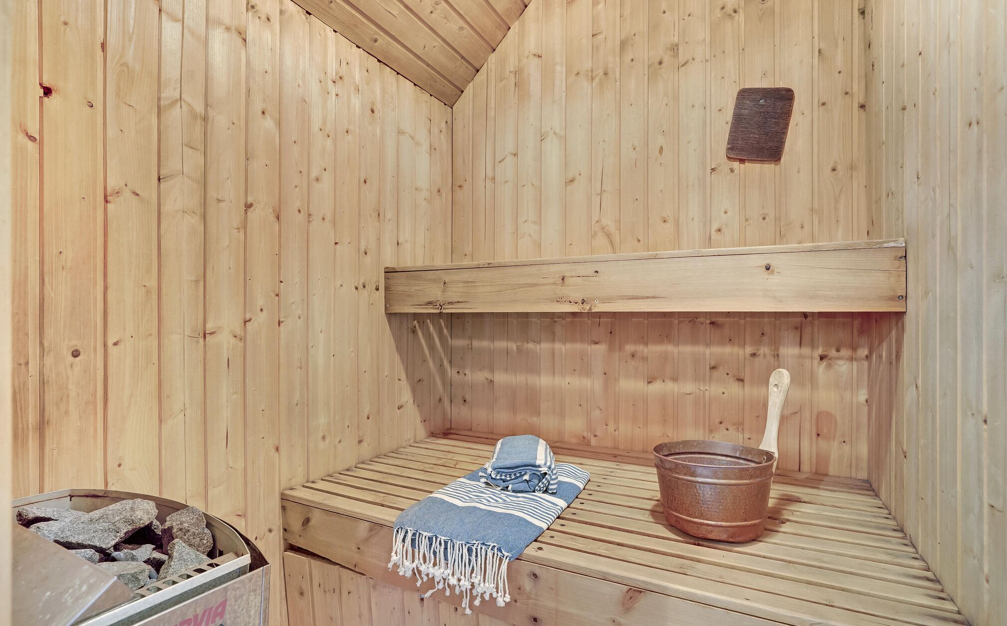 Una sauna con paredes de madera, un banco, una toalla y un cubo de madera.