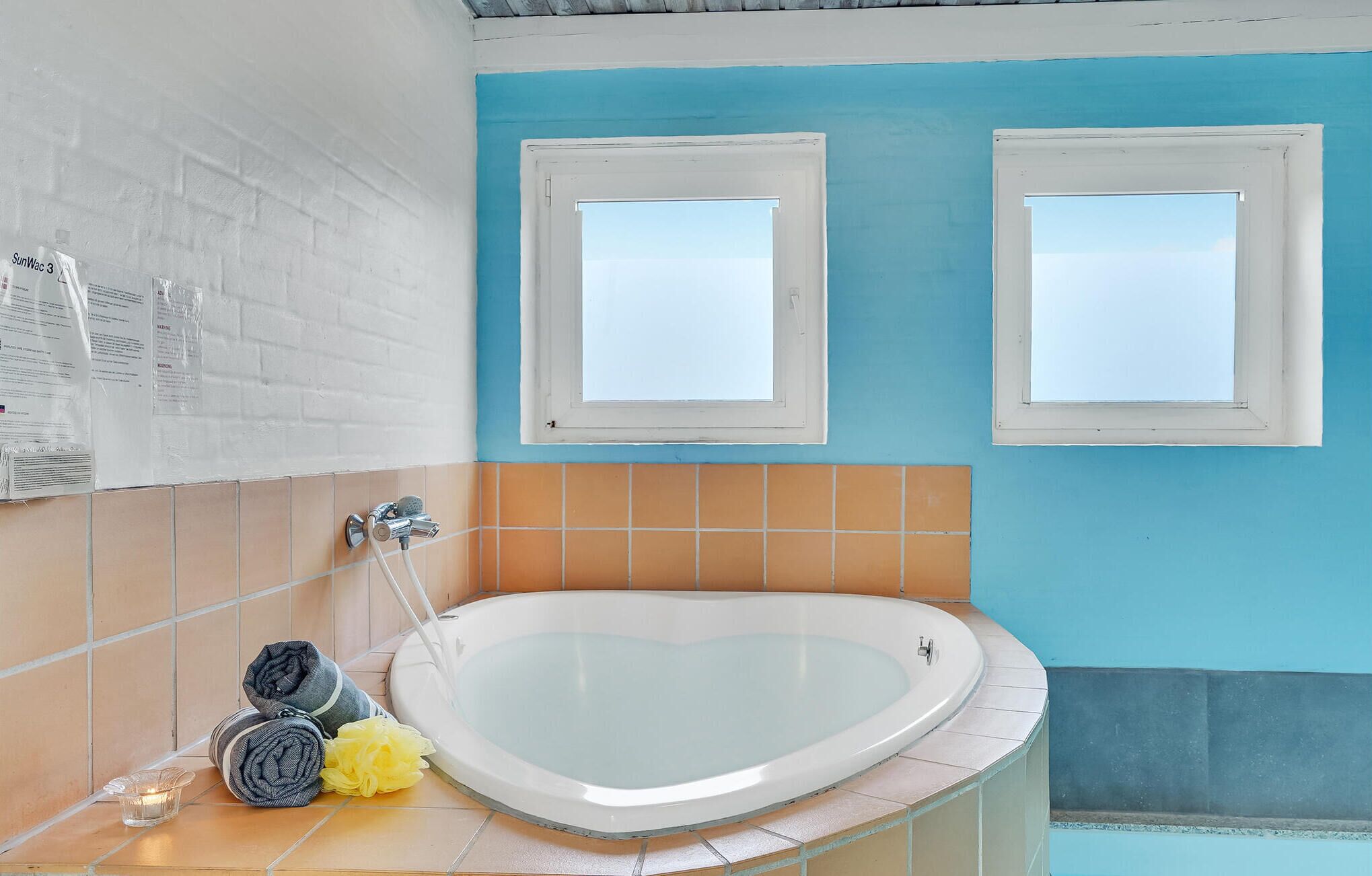 A bathroom with a heart-shaped bathtub, two windows, and a tiled wall.