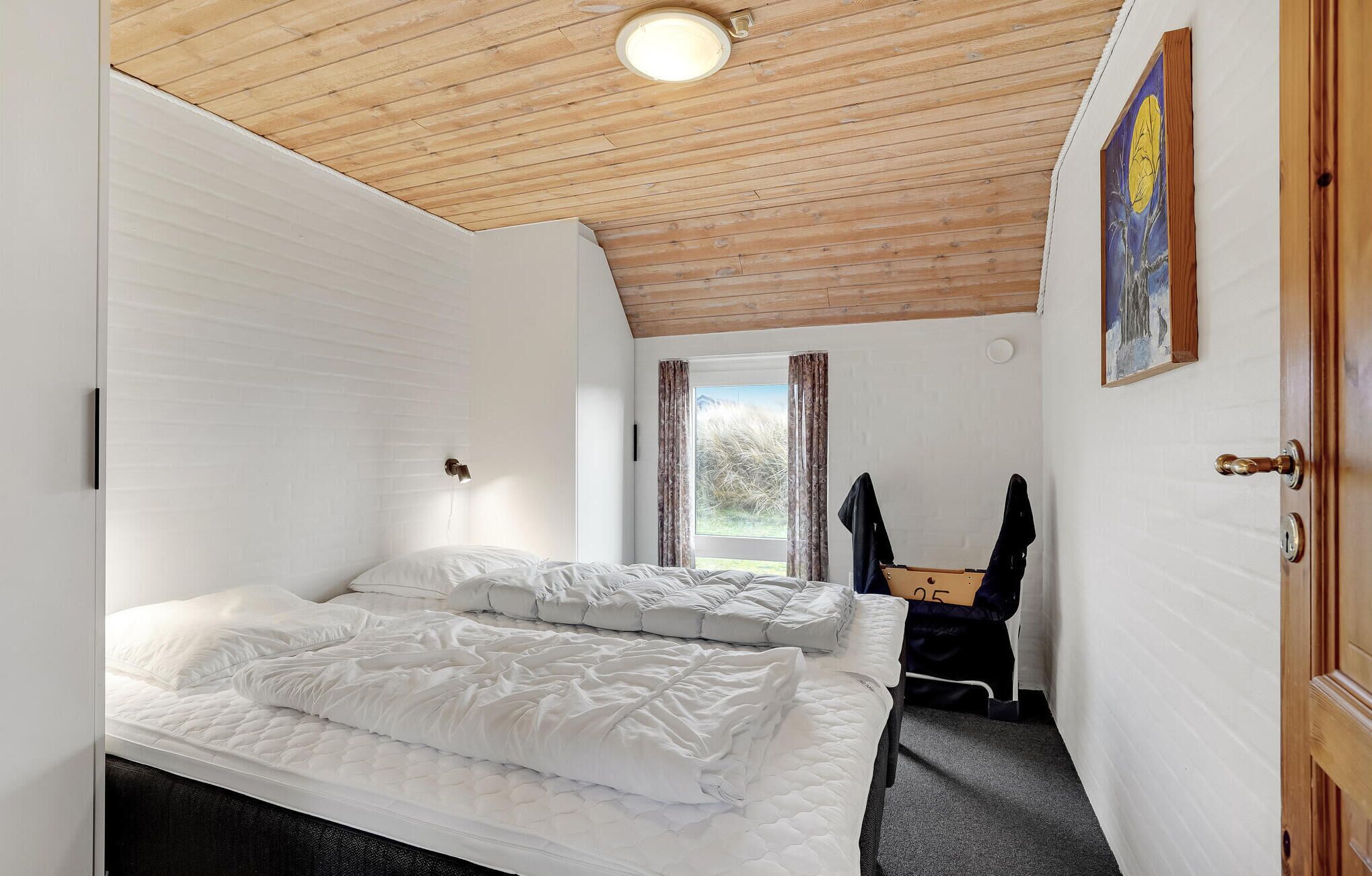 A bedroom with two beds, a wooden ceiling, a window with curtains, a door, and a painting on the wall.