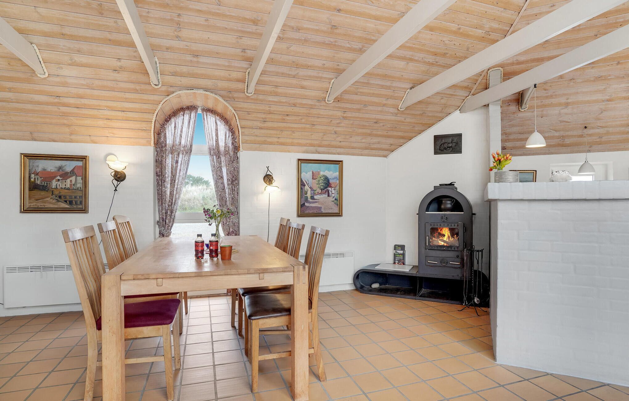 Un comedor con una mesa y sillas de madera, una chimenea y dos cuadros en las paredes.