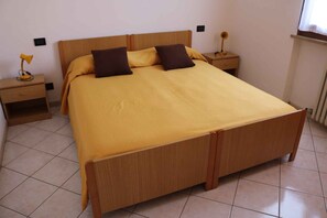 Ein Einzelbett mit Holzrahmen und gelber Bettdecke, an beiden Seiten mit Nachttischen und Lampen.