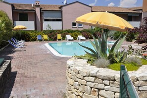 Ein Poolbereich mit Steinmauer, Pool und mehreren Liegestühlen und Sonnenschirmen.