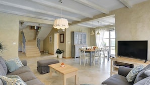 A spacious living room with a large TV, a dining area with a table and chairs, a staircase leading to another level, and a potted plant. - Luxurious home in Fazana with sauna (Fazana)