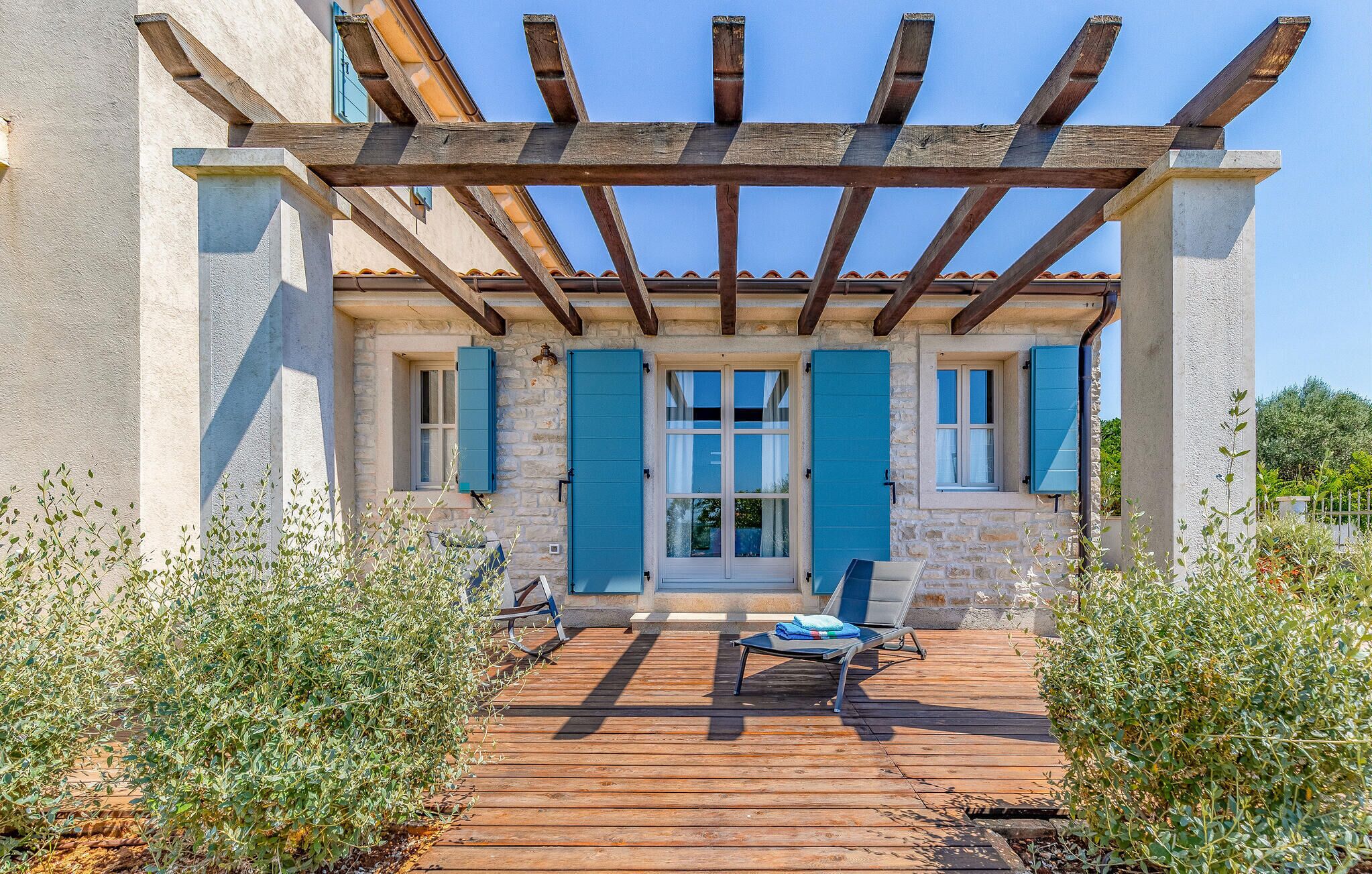 A covered outdoor area with a wooden deck, stone walls, and blue shutters.