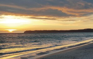 A beach with waves at sunset, a distant shoreline, and a clear sky.