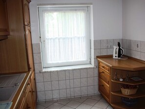 Eine Küche mit Fenster, Holzschränken, einer Fliesenrückwand und einer Kaffeemaschine auf der Arbeitsplatte.