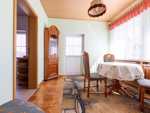A dining area with a table set for two, a wooden cabinet, and a chair with a cushion. - Holiday house Plauer Burgblick - holiday house (Plau am See)