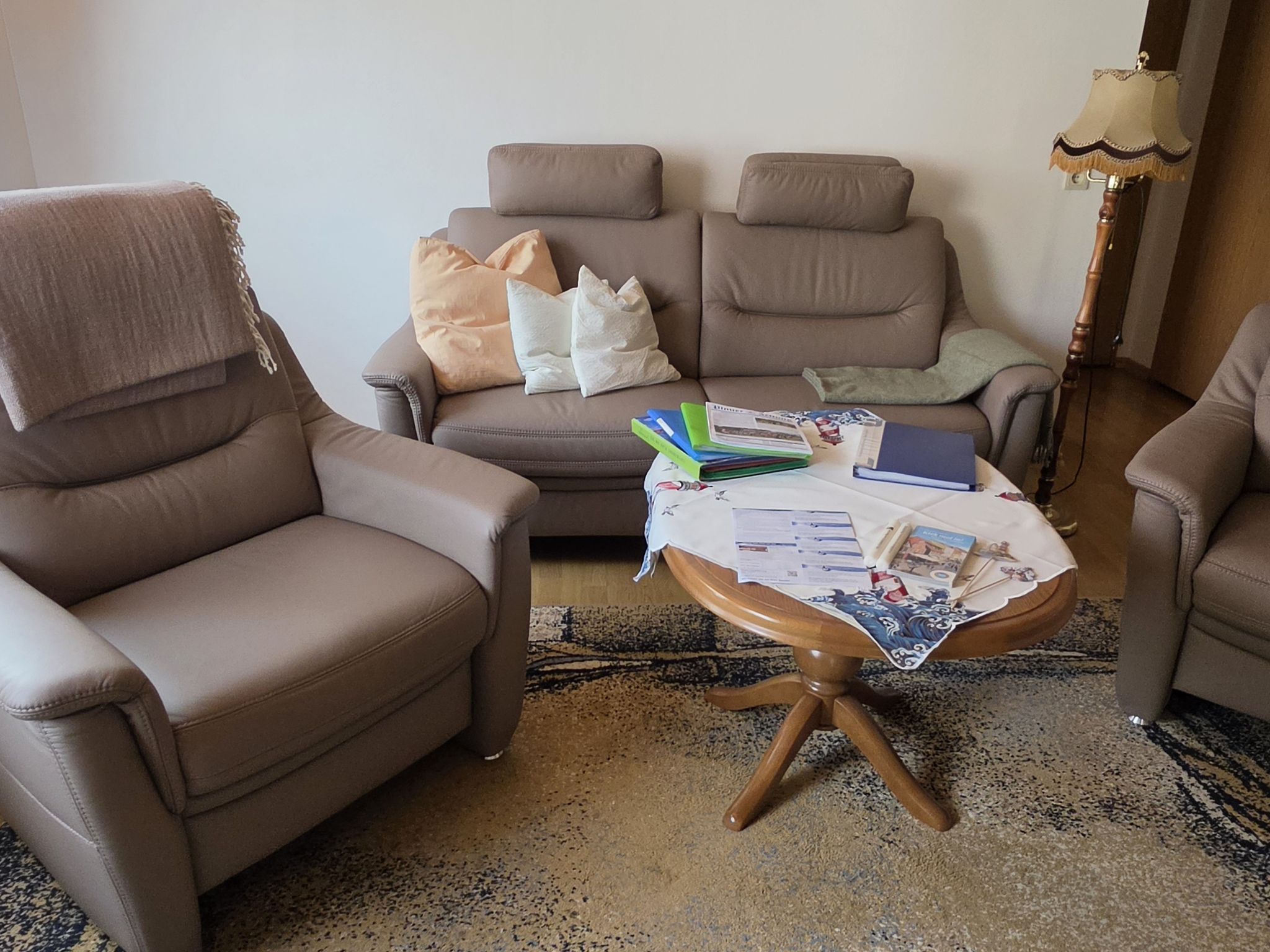 Ein Wohnzimmer mit zwei Sesseln, einem Sofa und einem kleinen Tisch mit Büchern und Papieren.