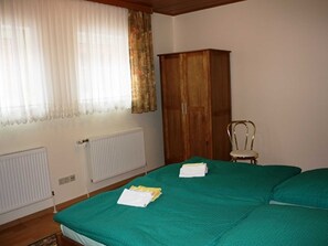Una habitación con cama, armario de madera, radiador y una silla.