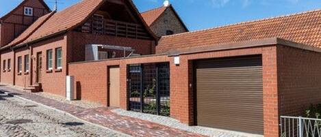 A brick building with a garage door, a paved driveway, and a cobblestone street.