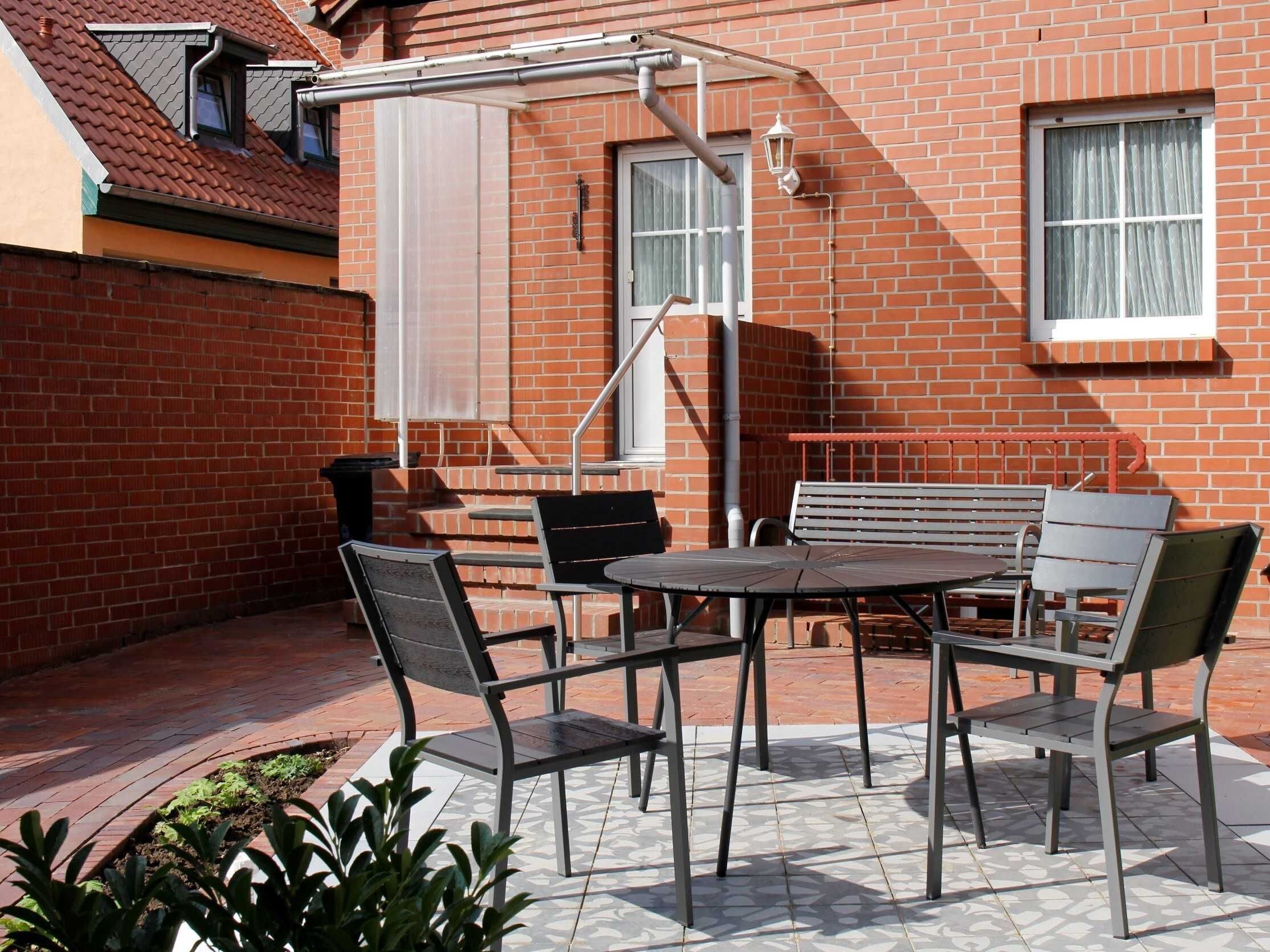 Un patio con una mesa redonda y cuatro sillas, una pequeña escalera y un muro de ladrillo.