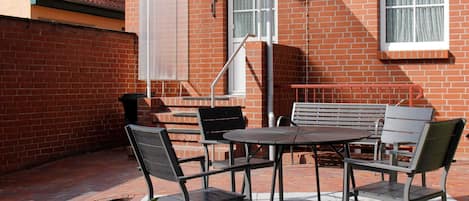 Un patio con una mesa redonda y cuatro sillas, una pequeña escalera y un muro de ladrillo.