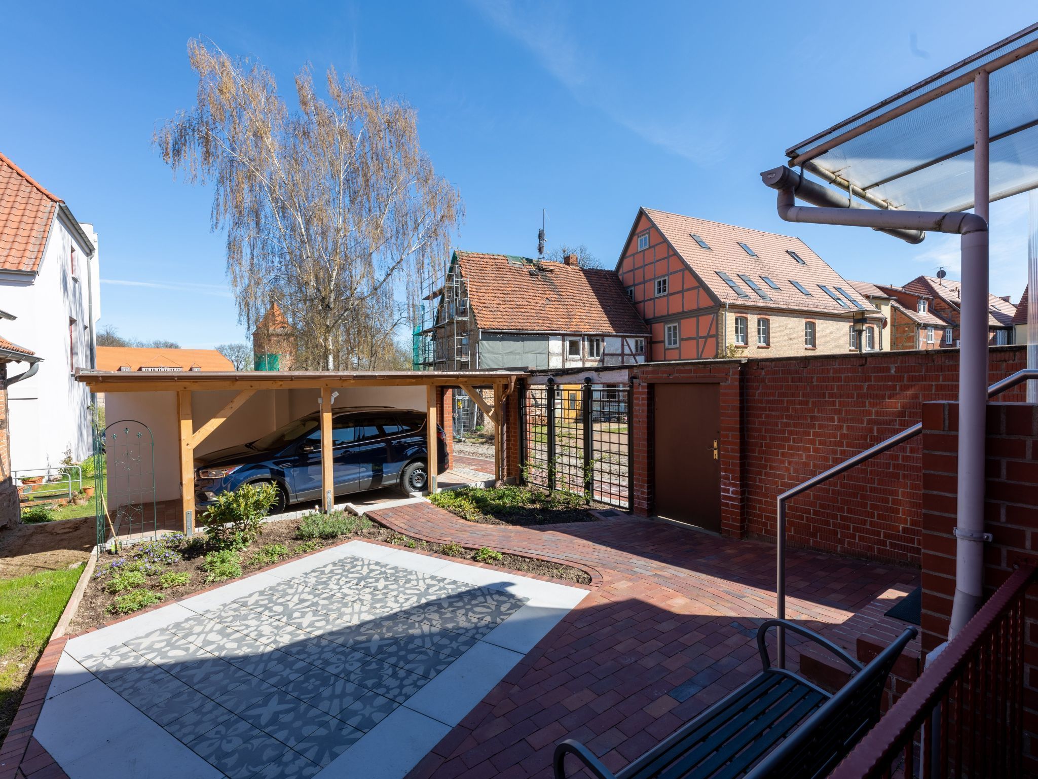 Ein Wohngebäude mit einem darunterliegenden Parkplatz, einem verschlossenen Eingangsbereich und einer gepflasterten Terrasse mit einem fugenlosen Fliesendesign.
