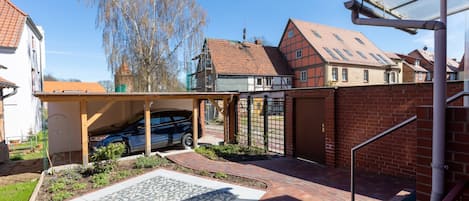 A residential property with a car parked under a covered area, a gated entrance, and a paved patio with a patterned tile design.