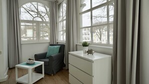 Une pièce avec un canapé gris, un bureau blanc et une fenêtre avec des rideaux.