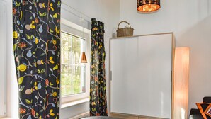 Ein Zimmer mit einem großen Fenster, einem weißen Kleiderschrank, einer hölzernen Bank und einer Stehlampe.