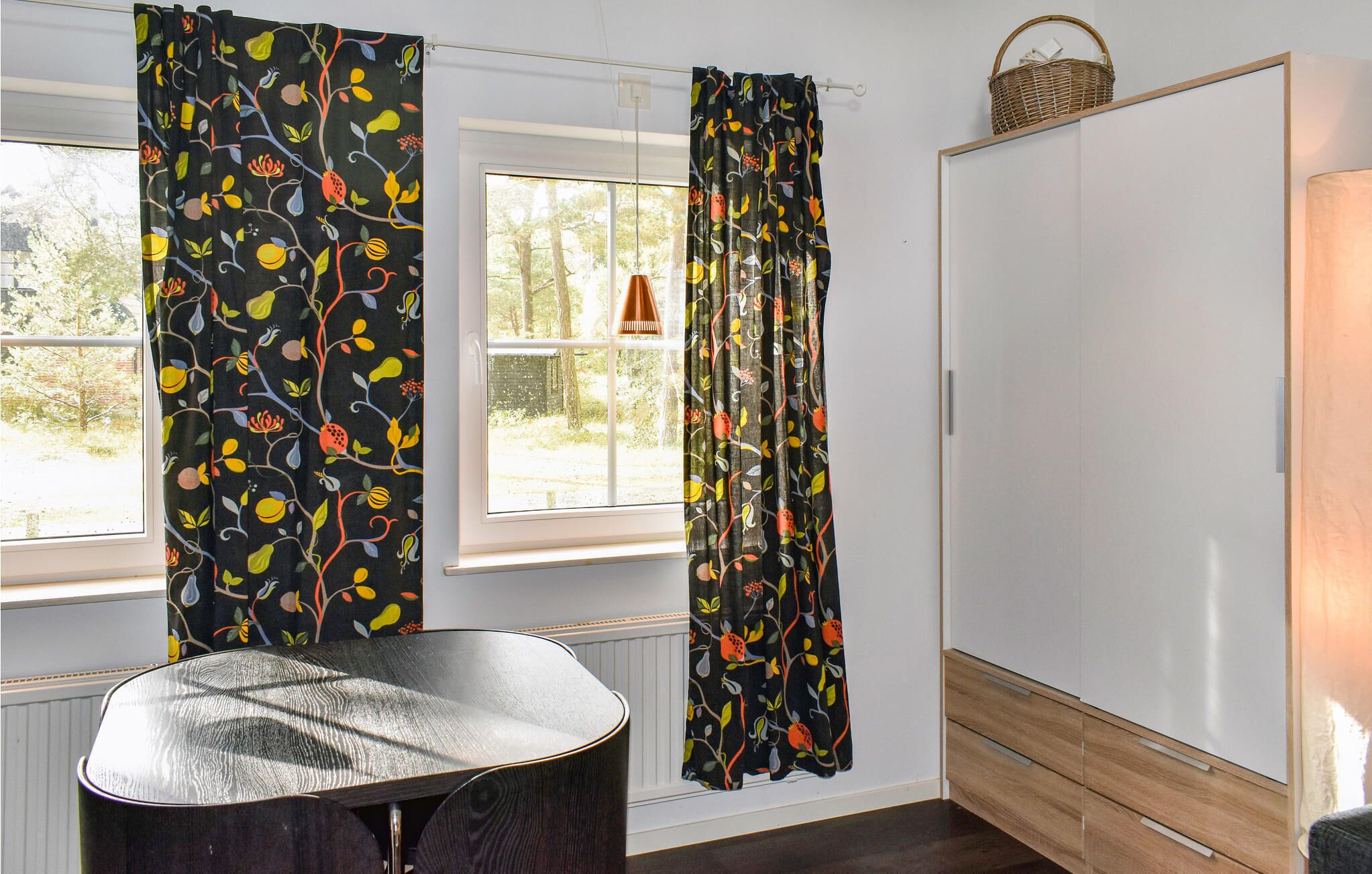 A room with a window, a chair, a wardrobe, and a basket on the wall.