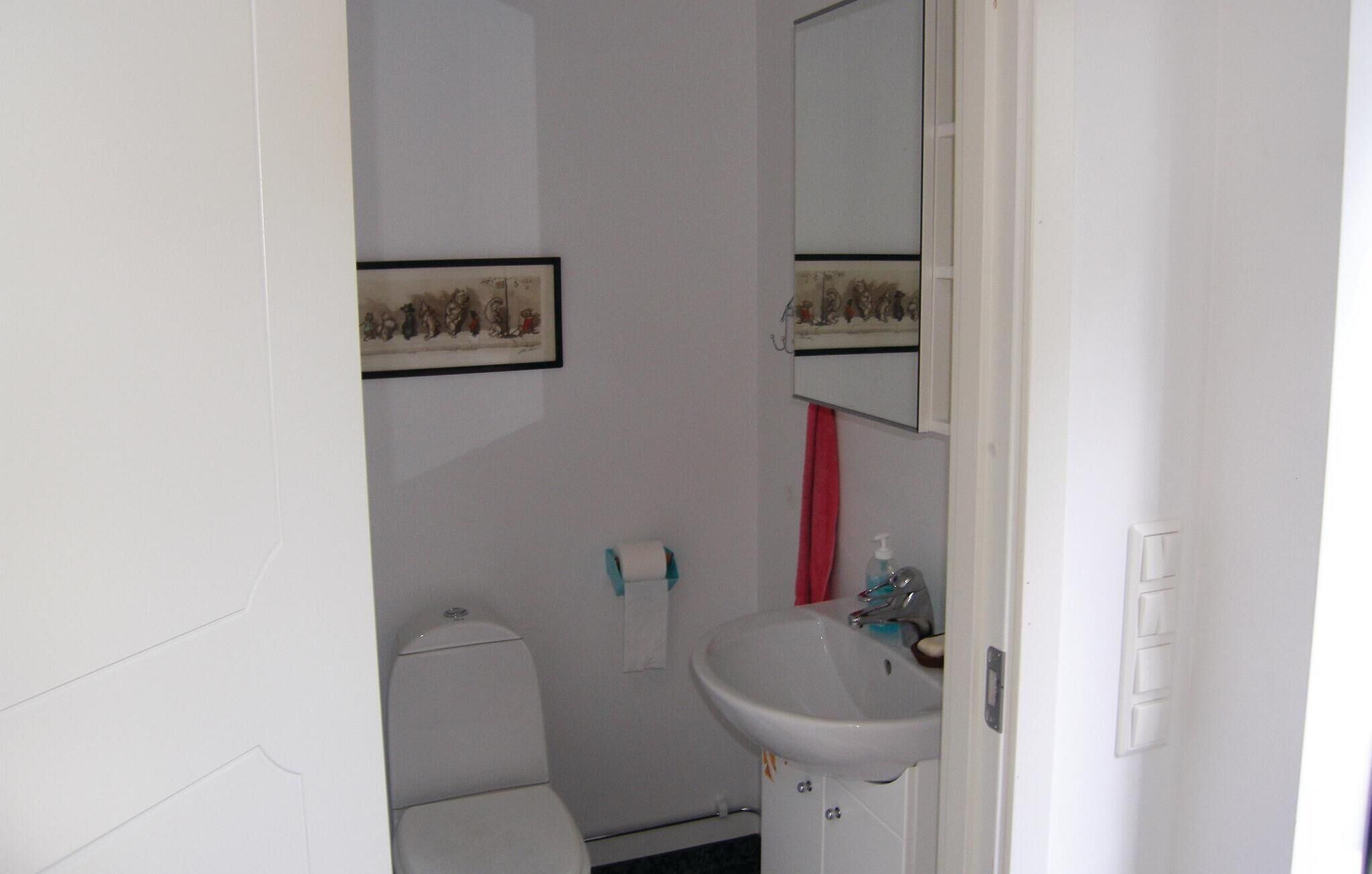 A small, basic bathroom with a toilet, sink, and a mirror. There is a framed picture on the wall above the toilet.