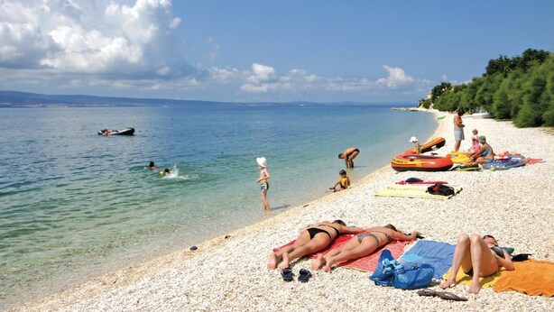 Ein Strand mit badenden und sonnenden Menschen.