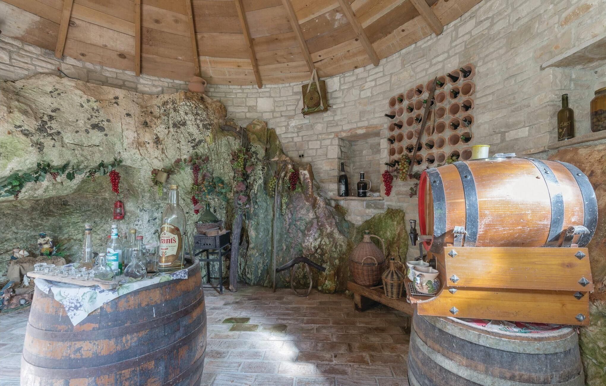 A rustic cellar with wooden barrels, stone walls, and a wine rack.