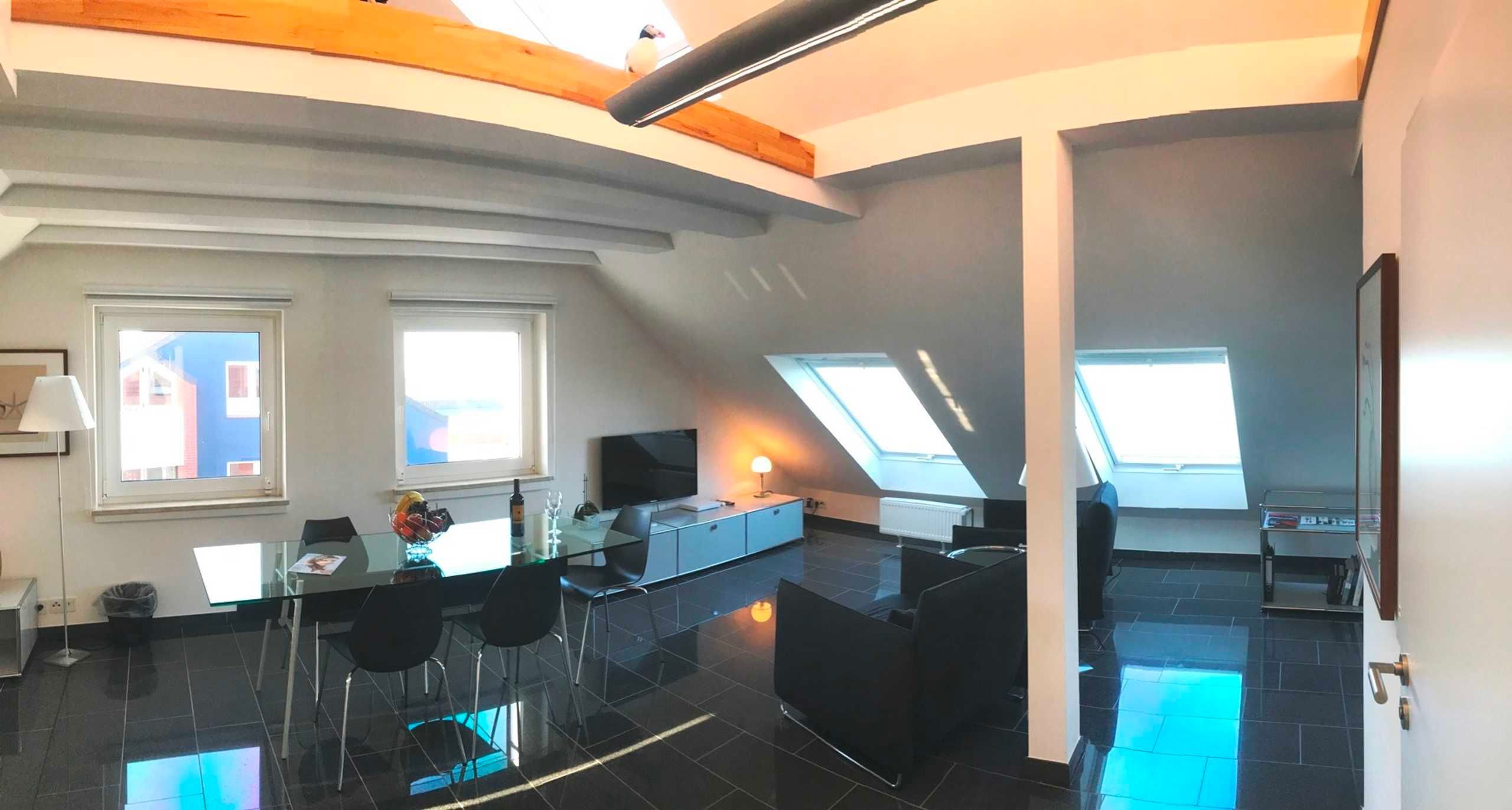 A modern interior with a dining area, kitchen, and living space, featuring skylights and a high ceiling.