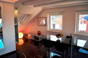 A modern dining area with a glass table, black chairs, a vase, and a lamp. - Nautilus Suite, 3rd floor, Studio / Loft Lakefront - Dune View Apartments (Helgoland)
