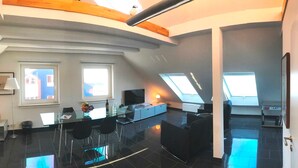 Un interior moderno con comedor, cocina y sala de estar, que cuenta con tragaluces y un techo alto.