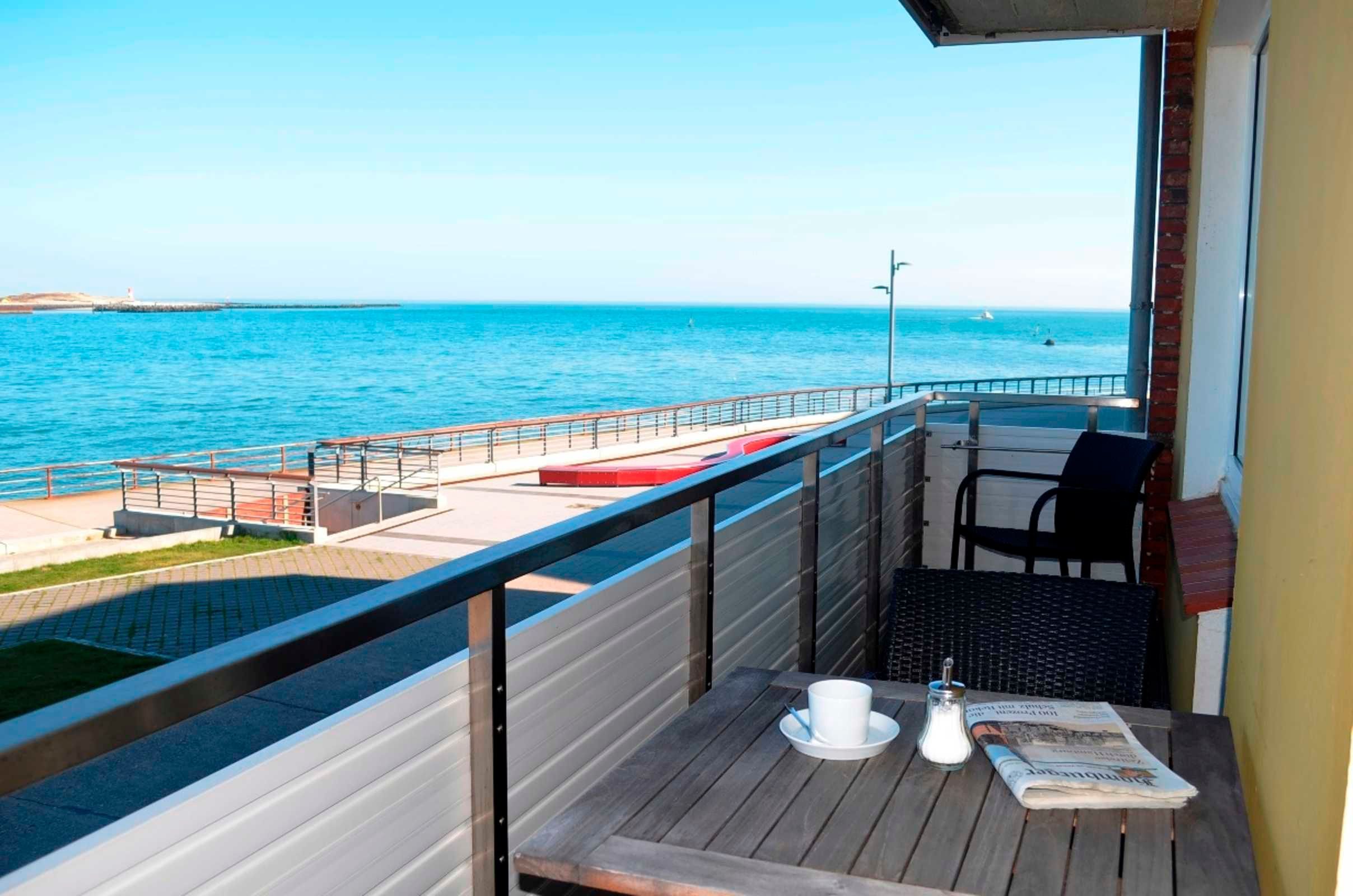 Un balcón con vista al mar, una mesa con un periódico y una silla.