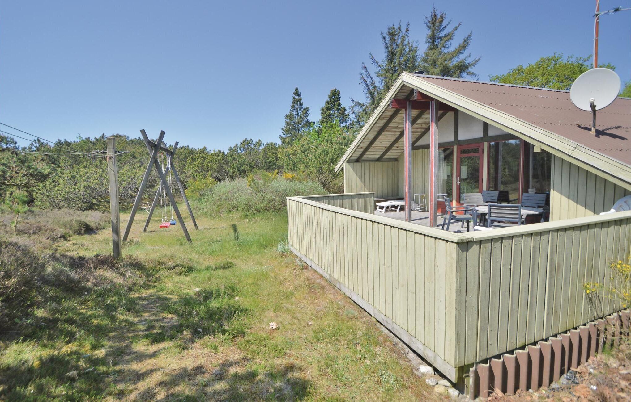 Een houten blokhut met een overdekte veranda, zitplaatsen buiten en een schotelantenne.