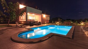 Una casa moderna con piscina, mobiliario exterior y un patio bien iluminado.